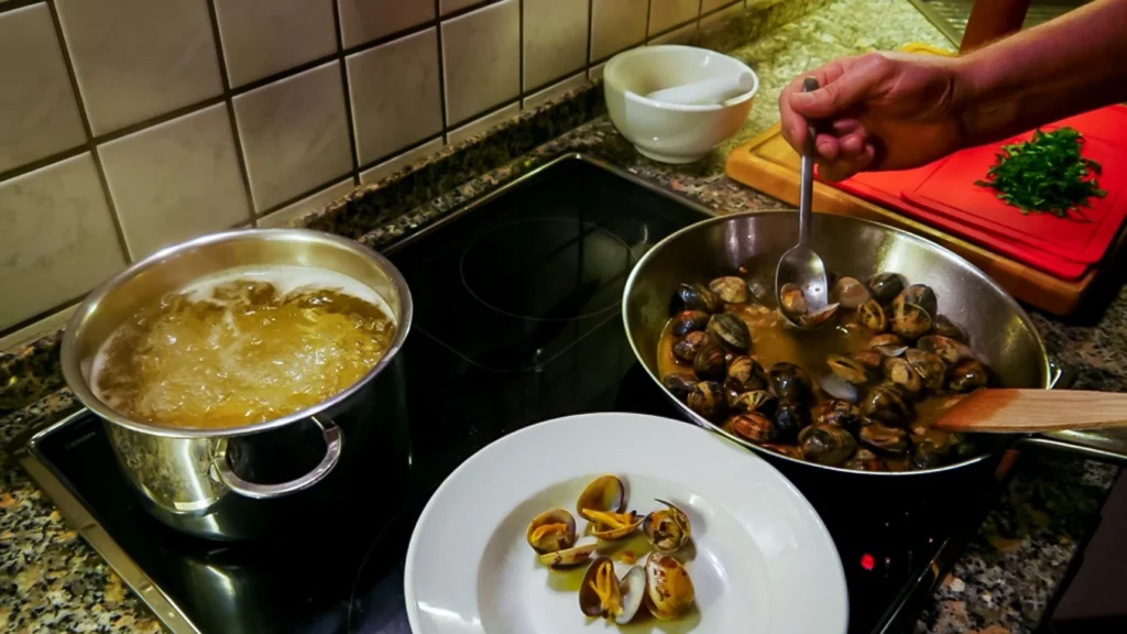 Ein Herd auf dem Nudeln in einem Topf kochen und in einer Pfanne Muscheln gedünstet werden